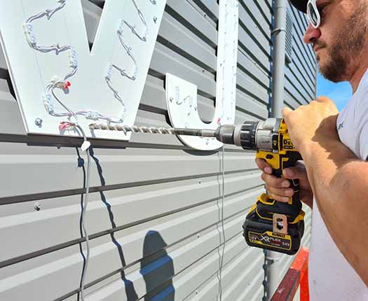 monteur bevestigt verlichte doosletters met aluminium behuizing en acrylaat front op een bedrijfsgevel bij daglicht